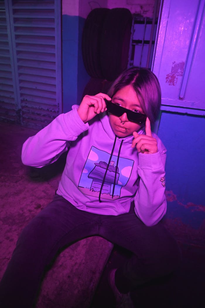 Young adult in vibrant hoodie with sunglasses, purple neon lighting, CDMX, urban style.